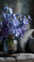 Vibrant blue flowers in a glass vase adorn a cozy gray sofa in a stylish interior setting photo