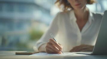 Person's Hand Writing on Document at Desk with Laptop photo