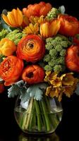 Bright orange floral bouquet with ranunculus, tulips, and greens arranged in a clear vase for a cheerful display photo