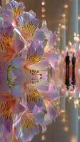 Elegant pink flowers reflect beautifully in calm water, showcasing a serene indoor setting with blurred figures in the background photo