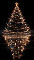 Glowing Christmas tree decorated with lights reflecting on dark water surface during festive season photo