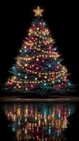 Glowing Christmas tree adorned with colorful ornaments reflecting on a surface at night during the holiday season photo