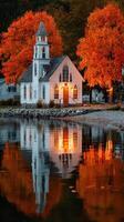 Charming white church reflected in calm waters surrounded by vibrant autumn foliage in a peaceful lakeside setting photo