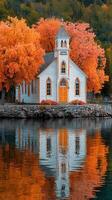 Charming white church reflects on calm water surrounded by vibrant autumn trees in a serene location photo