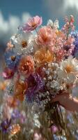 Vibrant bouquet of colorful flowers held against a blue sky in a sunny field during springtime photo