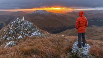 A person standing on a mountain top looking at the sunset photo