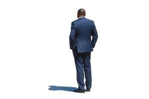 A man dressed in a formal blue suit stands with his back to the viewer. The solid white background highlights his figure, creating a striking visual contrast. photo
