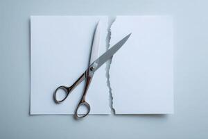 Scissors rest on a partially torn sheet of plain white paper on a clean surface, highlighting the act of cutting. The simple setup creates a focus on creativity and art. photo
