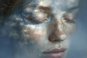 A young girl with closed eyes is portrayed in a peaceful expression. Clouds and a blue sky blend seamlessly across her skin, creating a dreamlike atmosphere that evokes tranquility and introspection. photo