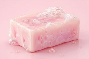 A glossy pink soap bar sits on a smooth, light surface with bubbly foam accumulating around it. The soft color highlights the soaps texture and freshness, inviting sensory experience. photo