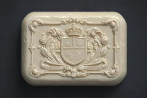 A luxurious bar of soap sits against a dark backdrop, showcasing intricate designs and a royal crest. The creamy texture is emphasized by its elaborate decorations, enhancing its visual appeal. photo