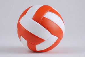 A volleyball featuring a vibrant pattern of orange and white stripes rests on a neutral gray background. The smooth texture highlights its design, suggesting readiness for play. photo