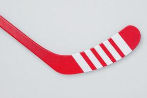 This red hockey stick features bold white stripes on the blade, positioned against a neutral gray background. The design highlights the sticks sleek shape and vibrant color. photo