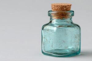The clear blue glass bottle sits on a light gray surface. Its vintage style is highlighted by a natural cork stopper, creating an elegant and simple display. photo