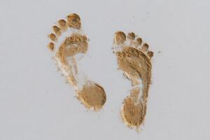 Fresh footprints are visible in fine sand, suggesting someone has recently walked along the shoreline. The light reflects off the sand, creating a peaceful beach atmosphere. photo