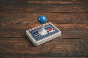 A classic arcade joystick with a blue ball top and vibrant striped design sits on a weathered wooden table. This nostalgic gaming controller evokes memories of vintage arcade games and playful times. photo