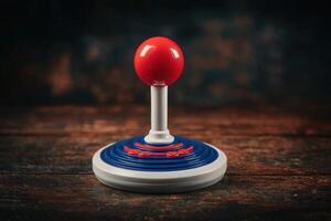 A classic joystick features a bright red ball atop a blue base, resting on a dark wooden surface. The ambient lighting emphasizes its vintage design, evoking memories of arcade gaming. photo