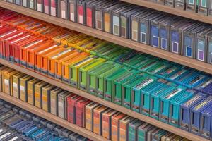 Colorful cassette tapes neatly arranged on wooden shelves display a vibrant spectrum. Each tape represents different music genres and memories, creating an inviting atmosphere for music lovers. photo