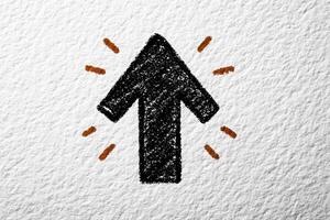 A bold upward arrow is drawn in black against a textured white background, surrounded by energetic orange accents. The design conveys a sense of direction and positivity. photo