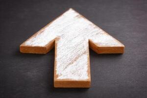 A wooden arrow shape rests on a dark background. The arrow is painted with white markings, emphasizing an upward direction. This simple yet effective design suggests guidance and progress. photo