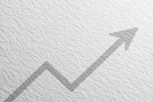 An upward arrow is depicted with a shadow effect, symbolizing growth or progress. The arrow is set against a lightly textured white background, enhancing visual depth. photo