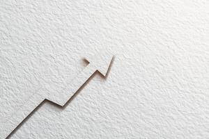 An upward arrow is intricately cut into textured paper, suggesting financial growth or progress. The simple yet striking design emphasizes the theme of upward momentum on a plain background. photo