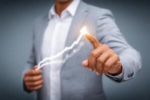 A business professional in a light grey suit points at an upward trending line graph. The background is softly blurred, emphasizing the subjects focus on growth and strategy in a modern setting. photo