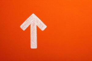 A large white arrow is painted on a vibrant orange wall, directing attention upwards. This striking design element enhances the visual appeal and guides viewers focus. photo