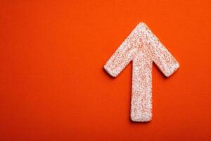 A textured white arrow points upward against a vibrant orange background, creating a bold visual contrast. The simplistic design emphasizes direction and movement in a straightforward manner. photo