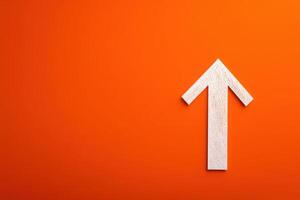A white wooden arrow points upward prominently displayed on a bright orange background. The contrast creates an eye-catching focal point that conveys a sense of direction and positivity. photo