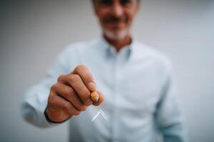 A man with gray hair and a smile uses a pencil to draw an arrow on an invisible surface. He stands in a well-lit indoor space, showcasing creativity and focus while engaged in his activity. photo