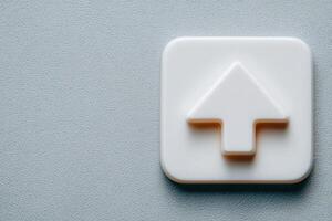 A simple white upload button icon sits prominently on a textured gray surface. The icon features an arrow pointing upwards, indicating a file upload function. photo