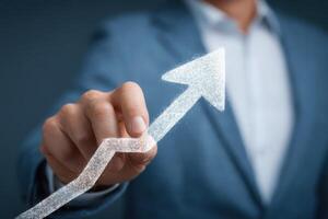 A business professional in a suit uses their hand to indicate a rising graph with an upward arrow, symbolizing growth and success during a corporate meeting or presentation. photo