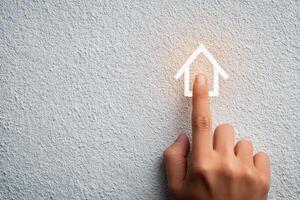 A hand with fingers extended is pressing on a glowing home icon drawn on a concrete wall. This interaction represents a concept of connectivity and digital interface. photo