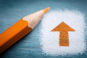 An orange pencil leans next to a painted upward arrow on a blue background. The arrow is prominently displayed, emphasizing direction and progression in a creative workspace. photo