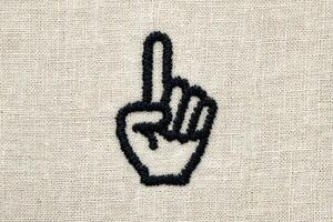 A hand with a raised index finger is embroidered on a beige fabric background. This gesture often signifies asking for attention or pointing out something important. photo