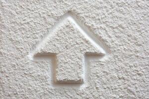 A close-up view of a textured white wall featuring a raised arrow shape. The design appears simple yet effective, implying direction or focus. photo