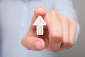 A hand is pointing upwards with a clear white arrow illustration, suggesting direction or highlighting a message. The neutral background and soft focus draw attention to the action. photo