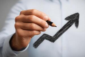 A business professional holds a pencil, drawing a rising graph on a blank surface. The action conveys a sense of progress and optimism in a corporate setting. photo