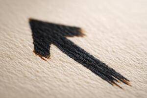 A striking black arrow is drawn with brush strokes on textured beige paper. The arrow points upward, conveying a sense of direction and movement in a simple yet effective design. photo