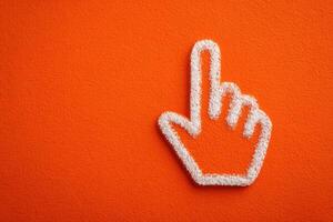 A hand gesture made of white material is prominently placed against a vibrant orange wall. The finger points upward, symbolizing focus or direction. This design creates a striking visual. photo