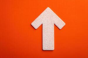 A large, textured arrow points upwards against a solid orange background, showcasing a minimalist design. The arrows surface has a subtle grain, adding depth to the composition. photo