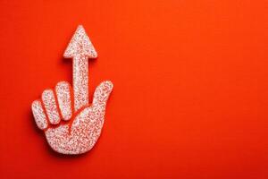 A hand gesture with a raised finger points upward against a vivid orange background. The textured hand is shown clearly, emphasizing the upward direction, suggesting importance or attention. photo