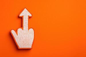 A hand shaped object with a raised finger is placed on a bright orange surface. The gesture is often used for emphasis or expression, making it visually striking and bold. photo