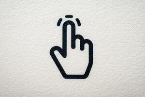 A simple black icon of a hand pointing upwards, suggesting a tapping or clicking action. The background features a light, textured surface, enhancing the symbols clarity and focus. photo