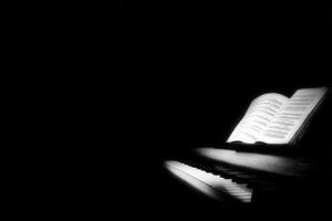 A piano sits in darkness, with only the sheet music glowing softly. The setting creates a serene atmosphere perfect for nighttime music practice or contemplation. photo
