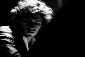 A young male performer is deeply focused while playing an instrument under dim lighting. Shadows accentuate his expressions, creating an intimate atmosphere in a live music setting. photo