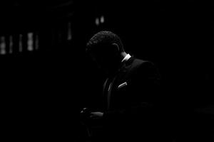 A well-dressed man in a suit is adjusting his cufflinks in a dimly lit environment, suggesting anticipation for an upcoming event. The focus is on his silhouette and refined attire. photo