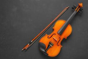 An orange violin and its bow are displayed neatly on a dark textured surface. The craftsmanship of the instrument and its shiny finish showcase its beauty and detail. photo