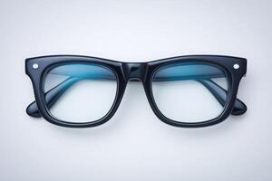 Black framed glasses with a sleek design rest on a neutral surface. The glasses feature blue-tinted lenses, creating a stylish contrast against the simple backdrop. photo